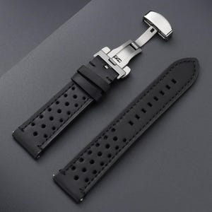 May include: Black leather watch strap with a stainless steel clasp. The strap features a perforated design and is shown unattached. The watch band is designed for durability and style.