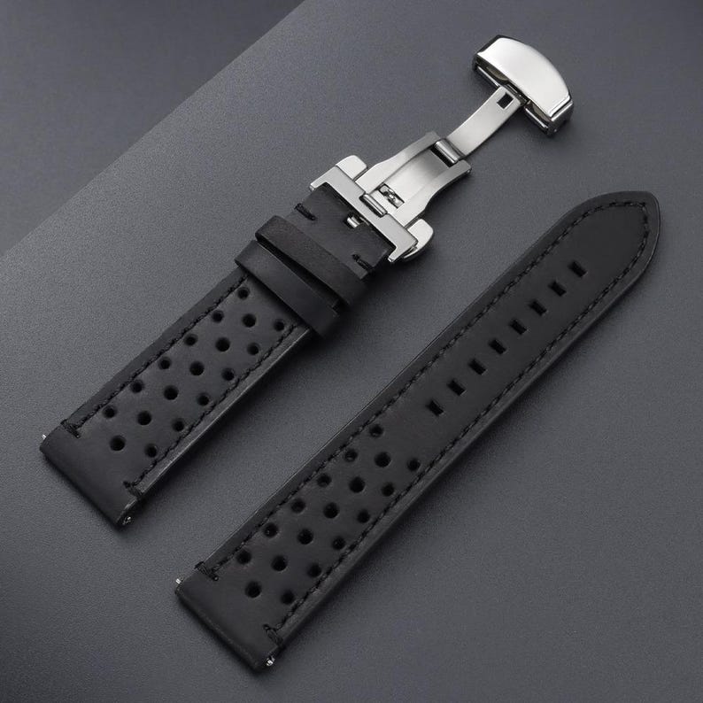 May include: Black leather watch strap with a stainless steel clasp. The strap features a perforated design and is shown unattached. The watch band is designed for durability and style.