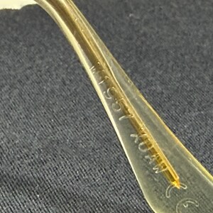 May include: A translucent yellow eyeglass temple arm featuring embossed text that reads 155 and CE. The material is smooth and semi-transparent, showing a thin internal structural wire running through the center of the curved plastic component.