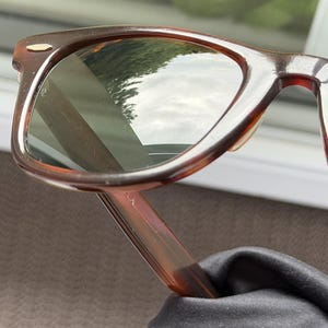 May include: Tortoiseshell-patterned sunglasses with dark-tinted lenses and a gold-tone metal accent on the upper corner of the frame. The frame features a classic rectangular shape with rounded edges and a smooth, polished finish throughout the structure.