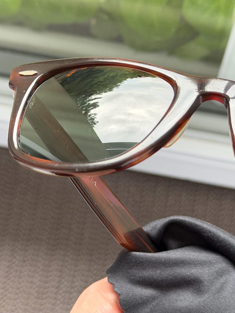 May include: Tortoiseshell-patterned sunglasses with dark-tinted lenses and a gold-tone metal accent on the upper corner of the frame. The frame features a classic rectangular shape with rounded edges and a smooth, polished finish throughout the structure.