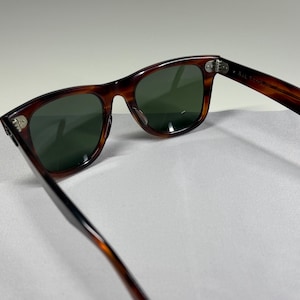 May include: Tortoiseshell-patterned sunglasses with dark green lenses and silver-toned metal hinges. The frames feature a classic rectangular shape with rounded edges, showcasing a brown and black mottled pattern throughout the plastic construction.