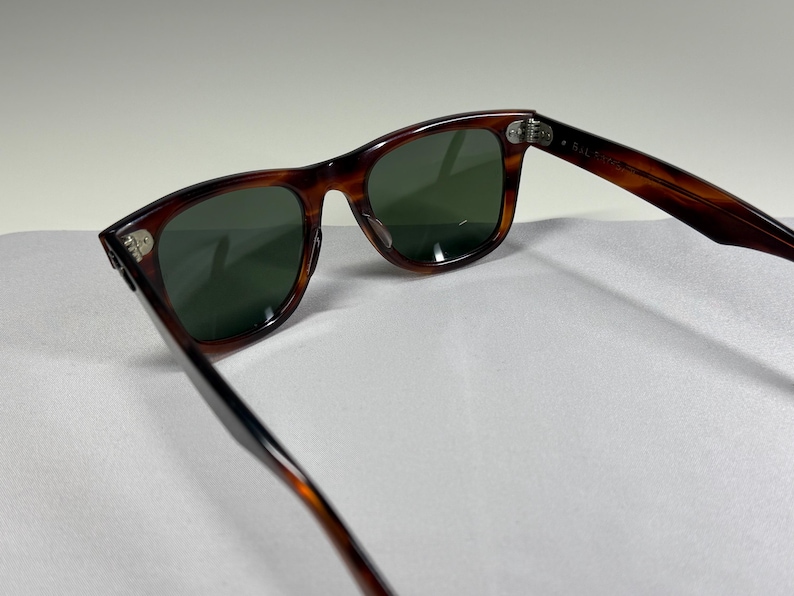 May include: Tortoiseshell-patterned sunglasses with dark green lenses and silver-toned metal hinges. The frames feature a classic rectangular shape with rounded edges, showcasing a brown and black mottled pattern throughout the plastic construction.