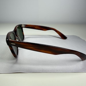 May include: Tortoiseshell-patterned sunglasses with dark green lenses and a classic frame shape. The temples feature a small silver-toned metal accent near the hinges, and the frame has a smooth, polished finish with a distinct brown and black pattern.