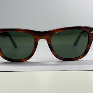 May include: Tortoiseshell-patterned sunglasses with a brown and black frame and dark green lenses. The frame features a classic wayfarer shape with silver-toned metal accents on the outer corners of the front rims, providing a distinct look.