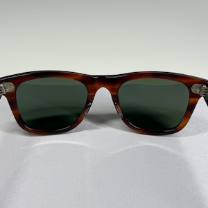 May include: Tortoiseshell-patterned sunglasses with dark green lenses. The inner left temple arm features the text Wayfarer, while the inner right temple arm displays B&L 5022. The frame has silver-toned metal hinges connecting the arms to the front.