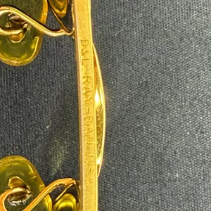 May include: Gold-toned metal eyeglasses frame featuring yellow-tinted nose pads. The bridge is engraved with the text B&L RAY-BAN U.S.A. The frame structure includes thin metal arms and wire components that connect to the nose pads.