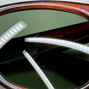 May include: Tortoiseshell-patterned sunglasses featuring dark green lenses. The frame has a polished finish with a visible silver-tone metal accent at the temple hinge. The lenses show light surface scratches and reflections of light strips.