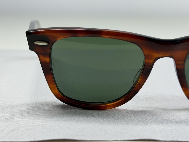 May include: Tortoiseshell-patterned sunglasses with dark green lenses. The frames feature a classic rectangular shape with a distinct brown and black mottled finish. A small, silver-toned metal accent is visible on the upper corner of the frame.