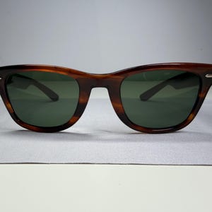 May include: Sunglasses with a brown tortoiseshell frame and dark green lenses. The frame features a classic wayfarer shape with silver-toned metal accents on the outer corners of the front rims, providing a clean and functional eyewear design.