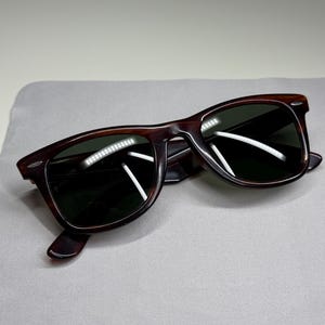 May include: Tortoiseshell-patterned sunglasses with dark green lenses and a classic rectangular frame shape. The frames feature silver-toned metal accents at the outer corners and temples, providing a distinct contrast against the brown pattern.