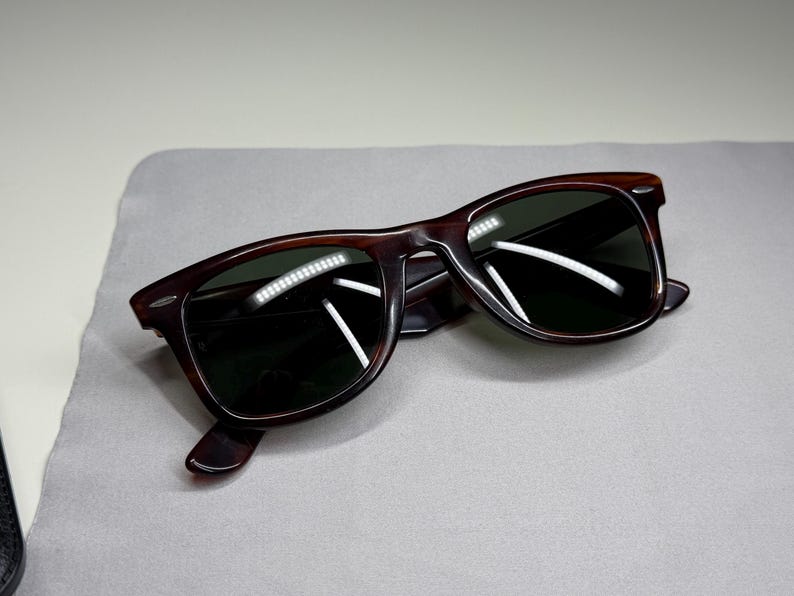 May include: Tortoiseshell-patterned sunglasses with dark green lenses and a classic rectangular frame shape. The frames feature silver-toned metal accents at the outer corners and temples, providing a distinct contrast against the brown pattern.
