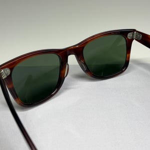 May include: Tortoiseshell-patterned sunglasses with dark green lenses and silver-toned metal hinges. The frames feature a classic rectangular shape with a smooth, polished finish. The temples are connected to the front frame by visible metal rivets.