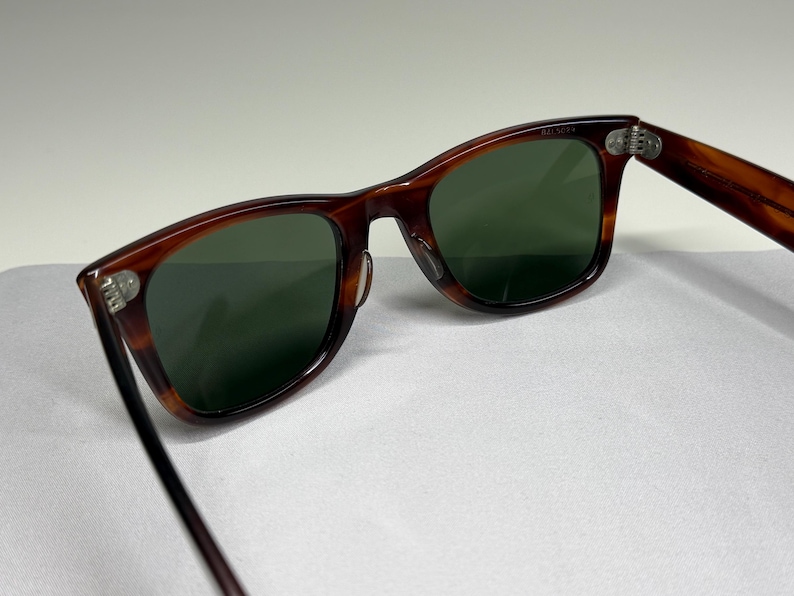 May include: Tortoiseshell-patterned sunglasses with dark green lenses and silver-toned metal hinges. The frames feature a classic rectangular shape with a smooth, polished finish. The temples are connected to the front frame by visible metal rivets.