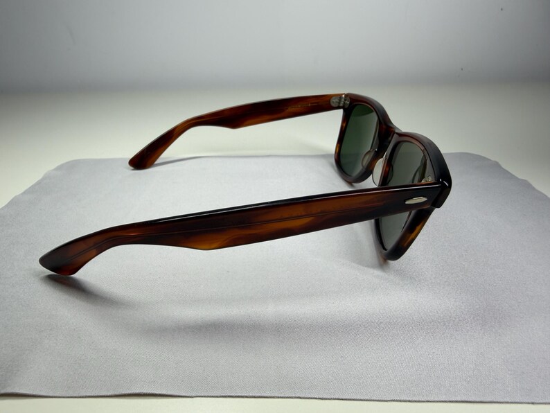 May include: Tortoiseshell sunglasses featuring a classic frame design with dark brown and amber mottled patterns. The eyewear includes dark green tinted lenses and silver-toned metal accents on the outer corners of the frame front.