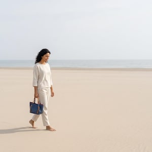 K&ouml;nnte beinhalten: Eine kleine, strukturierte marineblaue Handtasche mit beigen Ledergriffen und rotem Innenfutter, die ein minimalistisches Design mit rechteckigem Boden und zwei vertikalen Riemen aufweist, die von den Griffen nach unten verlaufen.