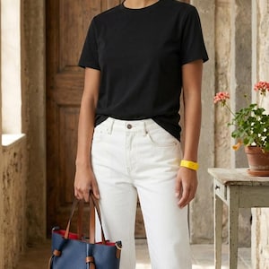 K&ouml;nnte beinhalten: Eine graue Baseballkappe, ein schwarzes kurz&auml;rmeliges T-Shirt, eine wei&szlig;e Jeans und eine marineblaue Beuteltasche mit braunen Lederriemen und einem leuchtend roten Innenfutter. Ein gelbes Armband wird am linken Handgelenk getragen.