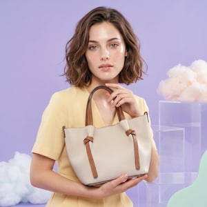 K&ouml;nnte beinhalten: Eine beigefarbene Handtasche aus Leder mit strukturierter Oberfl&auml;che, zwei braunen Ledergriffen und dekorativen braunen Lederknotendetails auf der Vorderseite. Die Tasche verf&uuml;gt &uuml;ber einen strukturierten Boden und eine weite &Ouml;ffnung.