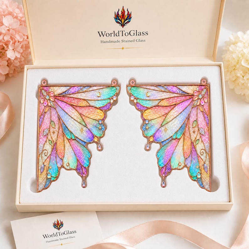 May include: Two stained glass fairy wings with iridescent pastel colors including pink, blue, and yellow, framed in copper. The wings are presented in a cream-colored box labeled WorldToGlass Handmade Stained Glass with a matching card.