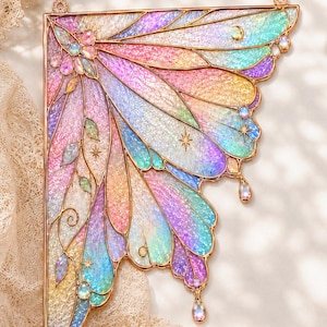 May include: A decorative wall hanging shaped like a single fairy wing with a gold metal frame. The wing features iridescent, multi-colored stained glass panels in shades of pink, blue, yellow, and green, accented with small star and moon charms.