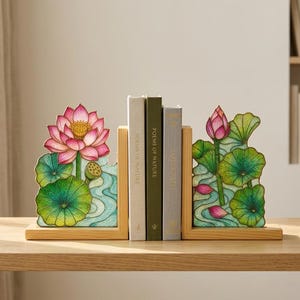 Pode incluir: Suportes de livros de madeira com um design de flor de lótus. Os suportes de livros apresentam uma flor de lótus rosa e amarela, folhas de nenúfar verdes e um design de água azul. Três livros são colocados entre os suportes de livros.