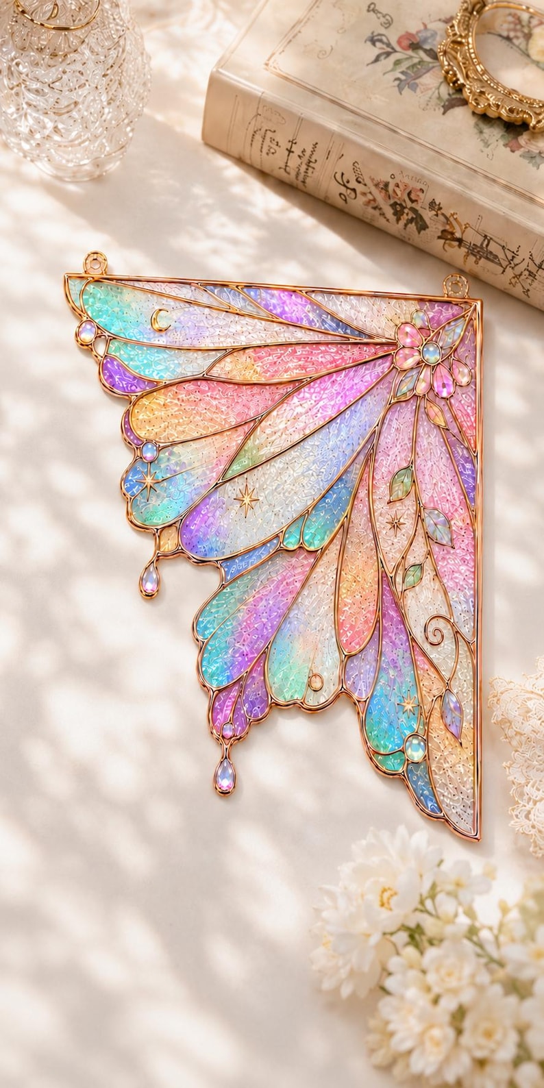 May include: A decorative wall hanging shaped like a single fairy wing with a gold metal frame. The wing features iridescent, translucent panels in shades of pink, blue, and yellow, accented with small star motifs, floral details, and hanging gems.
