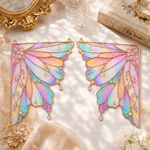 May include: A pair of decorative butterfly wings featuring a gold metal frame filled with iridescent, multi-colored resin in shades of pink, blue, yellow, and purple. The wings are adorned with small star and moon cutouts and dangling crystal accents.