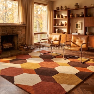 May include: A large area rug featuring a repeating geometric pattern of hexagons in shades of burnt orange, mustard yellow, dark brown, and cream. The rug is positioned on a dark wood herringbone floor in a room with two leather chairs.