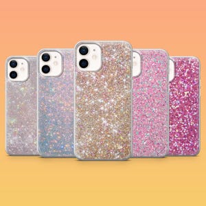以下が含まれることがあります： 一列に並んだ5つのスマートフォンケース。それぞれ異なるグリッター仕上げが施されています。シルバー、虹色のブルー、ゴールド、ライトピンク、濃いマゼンタのカラーバリエーションで、透明な縁取りとデュアルカメラ用の切り抜きがあります。