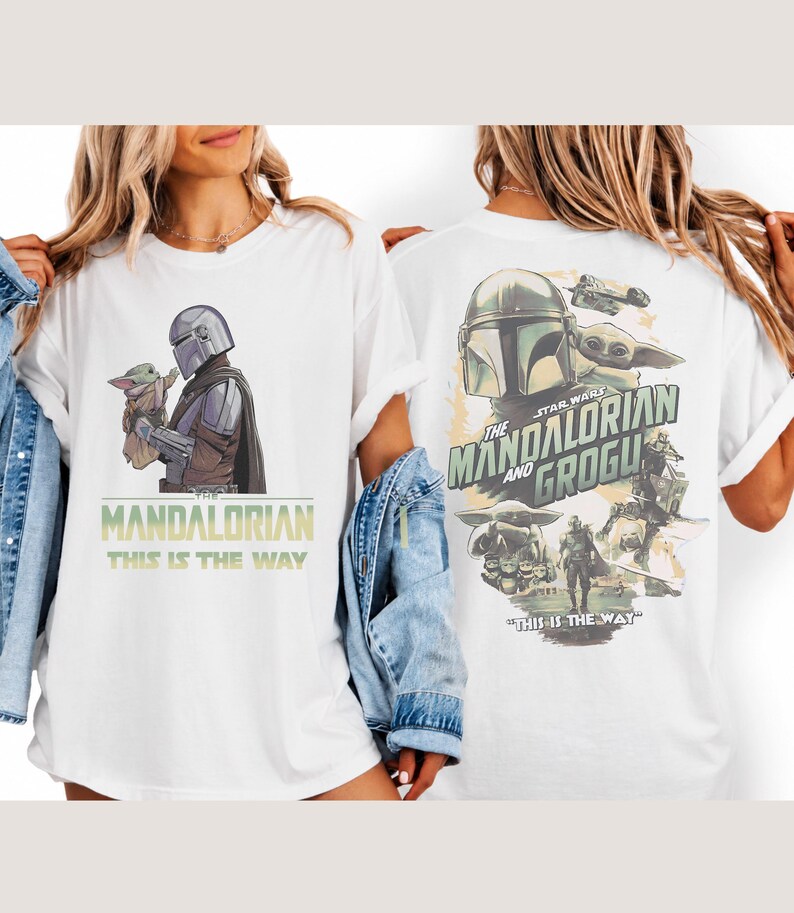 May include: A white t-shirt featuring Star Wars graphics. The front displays The Mandalorian holding Grogu with the text "The Mandalorian" and "This is the way". The back shows a collage of characters and vehicles with "The Mandalorian and Grogu" text.