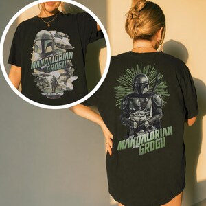 Puede incluir: Una camiseta negra con un estampado gr&aacute;fico de The Mandalorian y Grogu. La parte trasera muestra una gran ilustraci&oacute;n de los personajes con l&iacute;neas de estrella verdes y el texto The Mandalorian and Grogu. Un recuadro circular muestra el dise&ntilde;o frontal.