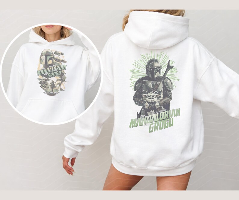 Puede incluir: Una sudadera con capucha blanca que presenta un estampado gr&aacute;fico de The Mandalorian y Grogu en la parte posterior y una versi&oacute;n m&aacute;s peque&ntilde;a en el frente. El dise&ntilde;o incluye a los personajes con armadura y t&uacute;nicas con texto verde.