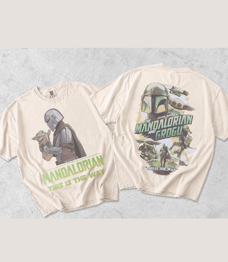 May include: Two off-white t-shirts featuring Star Wars graphics. The front shows The Mandalorian holding Grogu with the text "The Mandalorian This Is The Way". The back displays a larger collage of characters and the text "The Mandalorian and Grogu This Is The Way".
