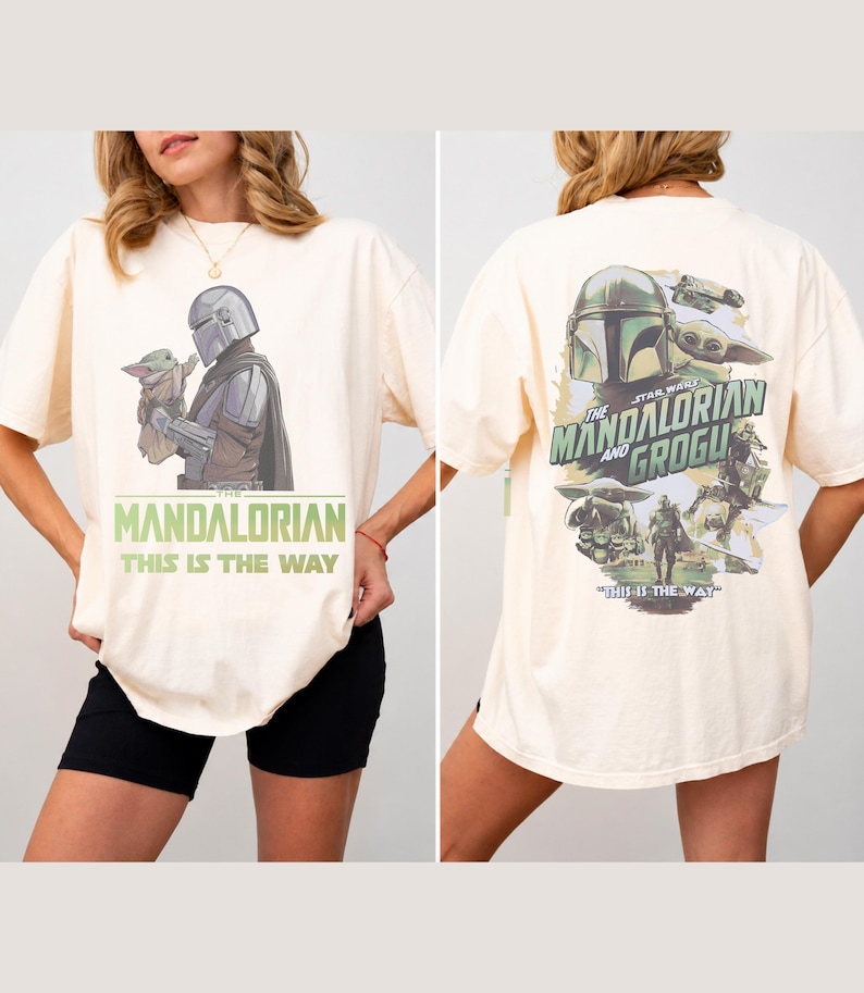 May include: An off-white t-shirt featuring a graphic of The Mandalorian and Grogu on the front with the text "The Mandalorian This Is The Way". The back displays a larger collage of the characters with the text "The Mandalorian and Grogu".