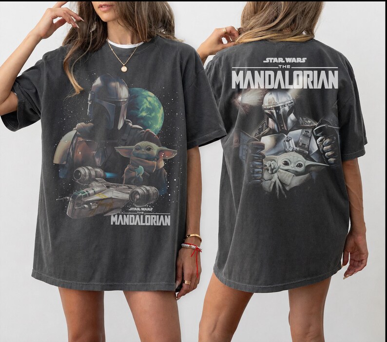 May include: A charcoal gray oversized t-shirt featuring a graphic print of The Mandalorian and Grogu. The front displays the characters with a spaceship and planet, while the back shows the characters with the text STAR WARS THE MANDALORIAN.