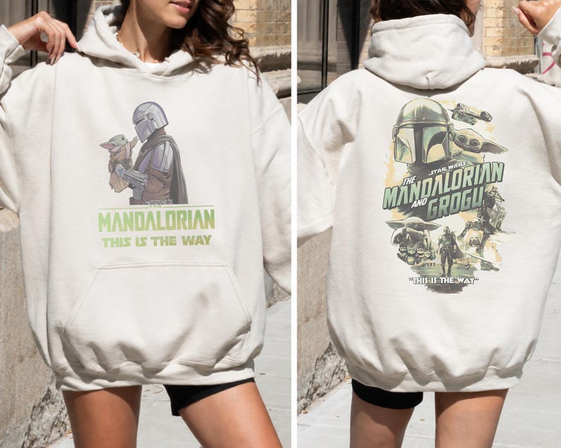 May include: An off-white hooded sweatshirt featuring a graphic of The Mandalorian and Grogu on the front with the text The Mandalorian This Is The Way. The back displays a larger, detailed collage of the characters and the text This Is The Way.