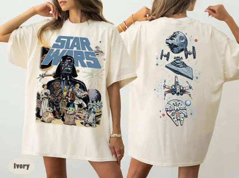 May include: An ivory t-shirt featuring a large Star Wars graphic on the front with Darth Vader, Luke Skywalker, Princess Leia, Chewbacca, and other characters. The back displays a vertical arrangement of space vehicles including the Death Star.