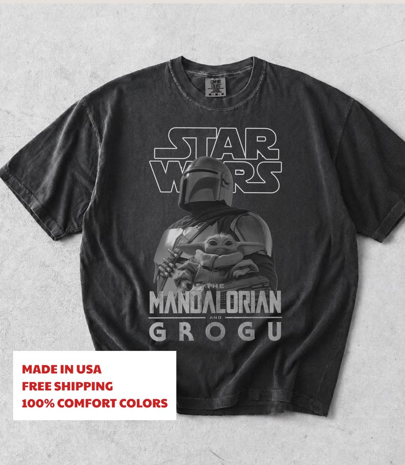 Może przedstawiać: Ciemnoszary t-shirt z kr&oacute;tkim rękawem z białym nadrukiem graficznym przedstawiającym Mandalorianina i Grogu. Nad postaciami znajduje się napis STAR WARS, a poniżej THE MANDALORIAN AND GROGU. Koszulka posiada okrągły dekolt.