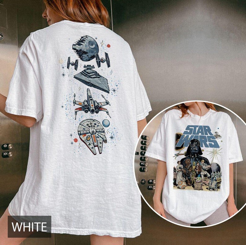 May include: A white t-shirt featuring a vertical graphic on the back with the Death Star, a Star Destroyer, an X-wing, and the Millennium Falcon. The front displays a Star Wars logo with Darth Vader and various characters in a group scene.