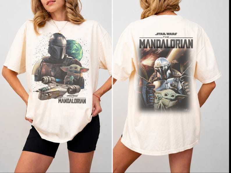 May include: An off-white t-shirt featuring a graphic print of The Mandalorian and Grogu. The front shows the characters with a spaceship and planet, while the back displays a larger action scene with the text Star Wars The Mandalorian.