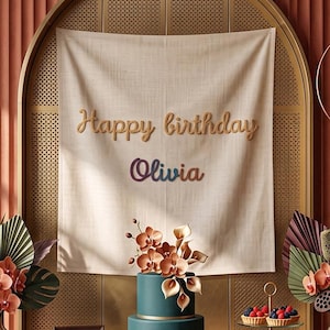 Könnte beinhalten: Ein cremefarbenes Stoffbanner mit dem Text Happy birthday Olivia in braunen und bunten Buchstaben. Das Arrangement umfasst eine zweistöckige blaugrüne Torte mit Orchideen, zwei Glasvasen mit getrockneten Palmblättern und eine Etagere mit Gebäck.