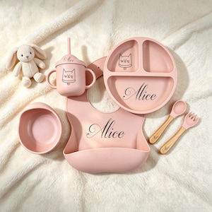 Könnte beinhalten: Ein rosa Silikon-Esslernset für Babys bestehend aus einem geteilten Teller, einer Schüssel, einem Lätzchen, einem Trinkbecher mit Strohhalm, einem Löffel und einer Gabel, personalisiert mit dem Namen Alice und einem Katzenmotiv. Ein Plüschhase.