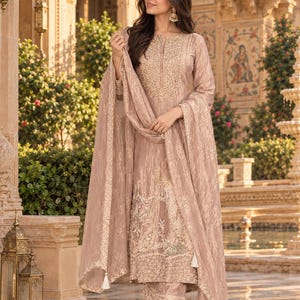 May include: A light brown long-sleeved tunic with intricate gold embroidery around the neckline and hem, paired with matching straight-leg trousers featuring embroidered cuffs and a coordinating sheer, patterned dupatta with tassel accents.