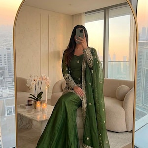 May include: A dark olive green three-piece ensemble featuring a long-sleeved tunic with intricate gold embroidery on the cuffs and hem, paired with wide-leg trousers and a matching sheer dupatta with gold border detailing and scattered motifs.