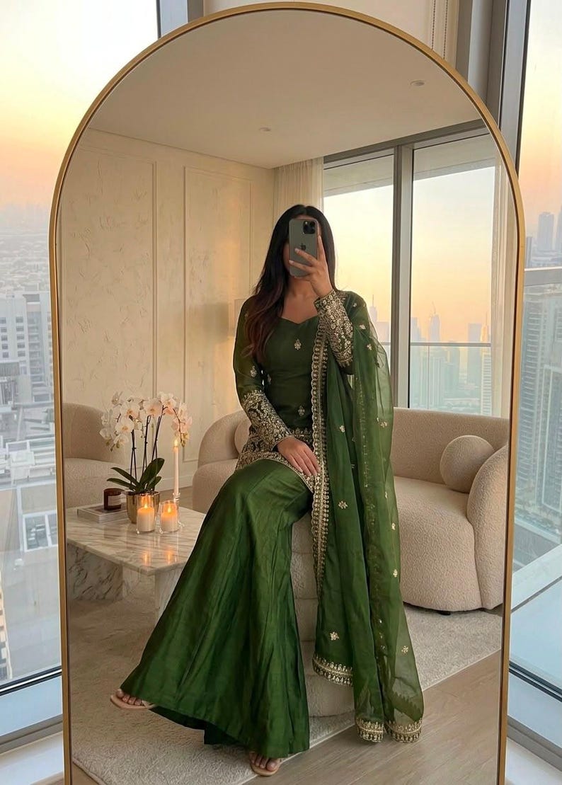 May include: A dark olive green three-piece ensemble featuring a long-sleeved tunic with intricate gold embroidery on the cuffs and hem, paired with wide-leg trousers and a matching sheer dupatta with gold border detailing and scattered motifs.