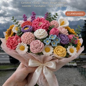 Könnte beinhalten: Ein Häkelblumenstrauß-Bündel mit verschiedenen Garnblumen, darunter Nelken, Gänseblümchen, Rosen, Vergissmeinnicht, Lavendel, Eukalyptus, Tulpen und Calla-Lilien. Der Strauß ist in hellrosa Papier eingewickelt und mit einem cremefarbenen Band gebunden.