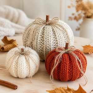 Puede incluir: Tres calabazas decorativas hechas de tela tejida en colores crema, blanco roto y naranja quemado. Cada calabaza presenta una textura acanalada vertical, un pequeño tallo de madera marrón en la parte superior y un trozo de cuerda de yute atado.