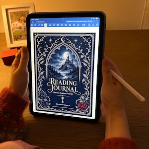 May include: A digital tablet displaying a reading journal cover with the text Reading Journal Between shadows & stories. The graphic features a dark blue castle under a full moon, surrounded by white floral vines and a single red rose.