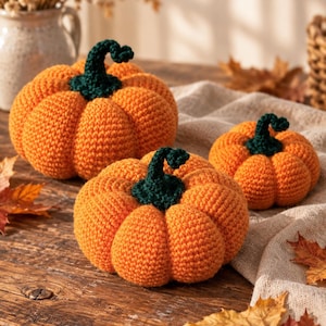 Op de afbeelding: Drie handgemaakte gehaakte pompoenen van fel oranje garen met donkergroene stelen. De pompoenen hebben een gestructureerd ribbelpatroon en zijn in een groep gerangschikt, wat hun ronde vormen en de gekrulde groene stelen goed laat zien.