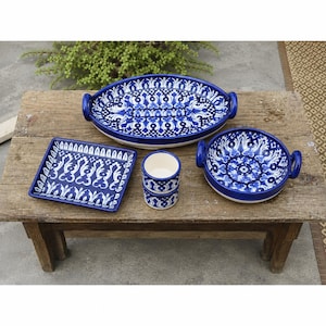 May include: A collection of ceramic tableware featuring a blue and white pattern. The set includes an oval platter with two handles, a square plate, a round bowl with two handles, and two small stacked cylindrical cups with a plain white interior.